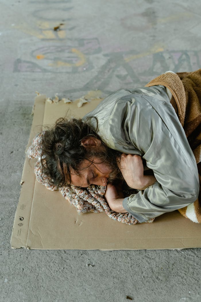 who-we-are Homeless man sleeping on a cardboard in an urban setting.
