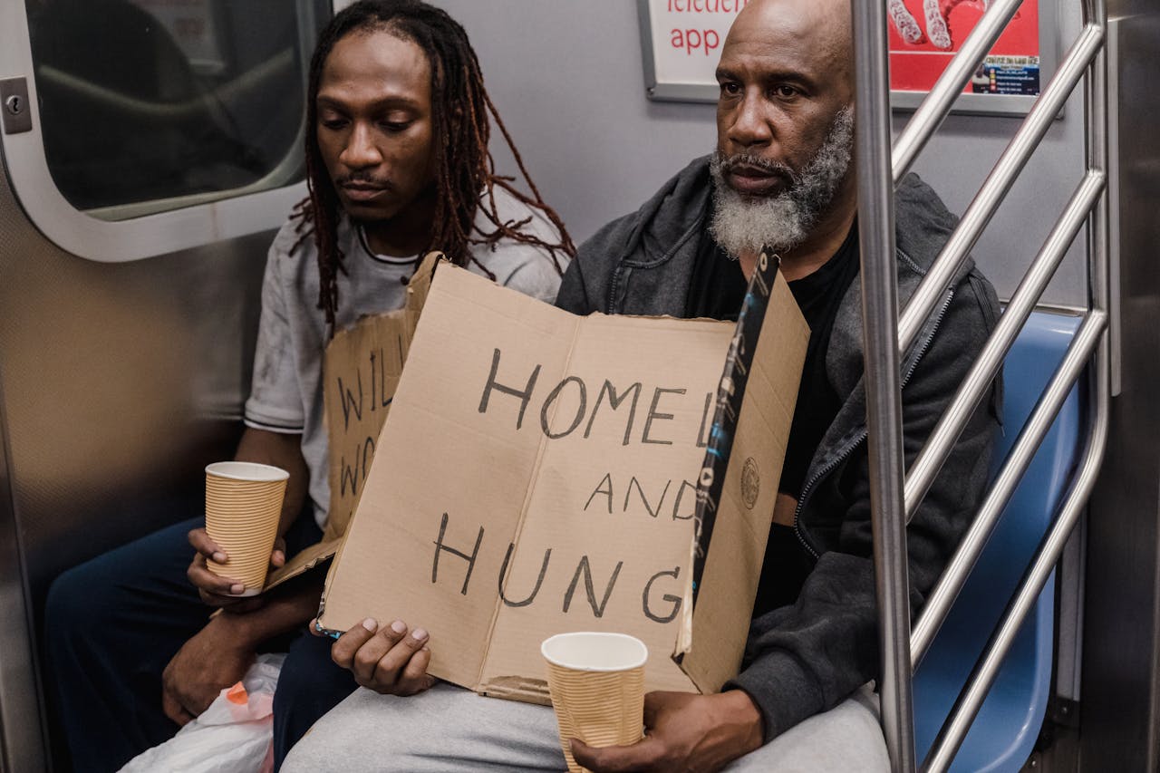 about-us Two men holding signs about homelessness in a subway train emphasize urban hardship.